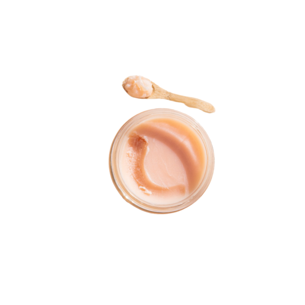 Un pot en verre contenant le Baume de nuit réparateur Overnight Repair Balm-50 ml de Cut by Fred, à la texture crémeuse et rose clair, est surmonté d'une petite cuillère en bois. La cuillère contient une noisette de baume, le tout sur fond blanc pour mettre en valeur sa texture soyeuse.