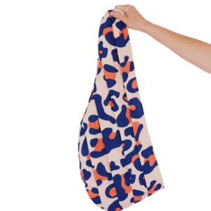 Une main tient un sac orné d'un motif coloré de formes abstraites bleues et orange sur fond clair, rappelant l'énergie vibrante de Turban By Fred – Pré-sécher les cheveux – Cut by Fred. Le sac est présenté sur un fond blanc uni.
