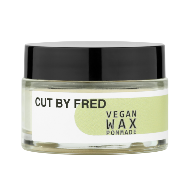 Un petit pot transparent au couvercle noir contient la pommade à la cire végétalienne Cut by Fred (50 g). L'étiquette, fidèle au style vegan du soin hydratant cheveux, arbore un design minimaliste avec des nuances vertes et un texte noir.