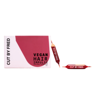 Une boîte étiquetée « Vegan Hair Impulse - complément pousse cheveux - Cut By Fred » avec une capsule rouge à côté et une autre verticale, toutes deux marquées du nom du produit.