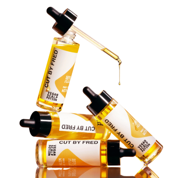 Quatre flacons de « Vegan Hair Impulse - complément pousse cheveux - Cut By Fred (Copie) » sont empilés avec art, un compte-gouttes délivrant l'huile. Les flacons transparents, aux bouchons noirs et aux étiquettes blanches, se détachent sur le fond blanc.