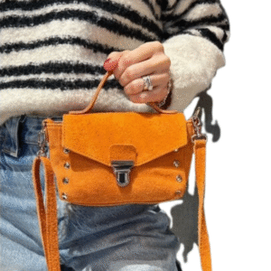 Une personne vêtue d'un pull rayé noir et blanc et d'un jean bleu tient le Petit sac à bandoulière en daim -Orange, un sac à bandoulière en daim orange avec des accessoires argentés.