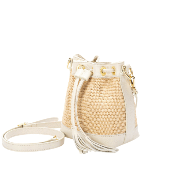 Le Sac Raphia et cuir véritable - Bandoulière réglable-Vanille est un petit sac croisé de type seau avec des panneaux de paille tressée, des garnitures en cuir vanille, des ferrures dorées, un cordon de serrage et une sangle amovible, sur fond blanc.
