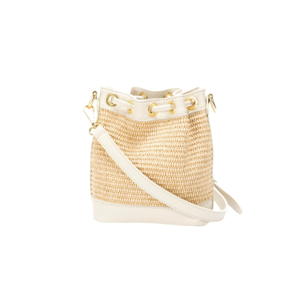 Le Sac Raphia et cuir véritable - Bandoulière réglable-Vanille est un sac seau tissé beige avec des bordures en cuir blanc, des œillets dorés et une bandoulière blanche réglable, présenté sur un fond blanc uni.
