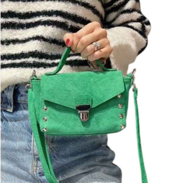 Une personne vêtue d'un pull rayé noir et blanc et d'un jean bleu tient le Petit sac à bandoulière en daim -Vert, doté d'une poignée supérieure, de clous argentés et d'une bandoulière.