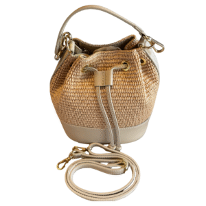Le Sac à main bandoulière raphia garni cuir-Taupe est un petit sac seau en paille tressée avec des bordures en cuir taupe, un cordon de serrage, des accessoires en métal doré et une bandoulière amovible en cuir assorti, le tout sur fond blanc.