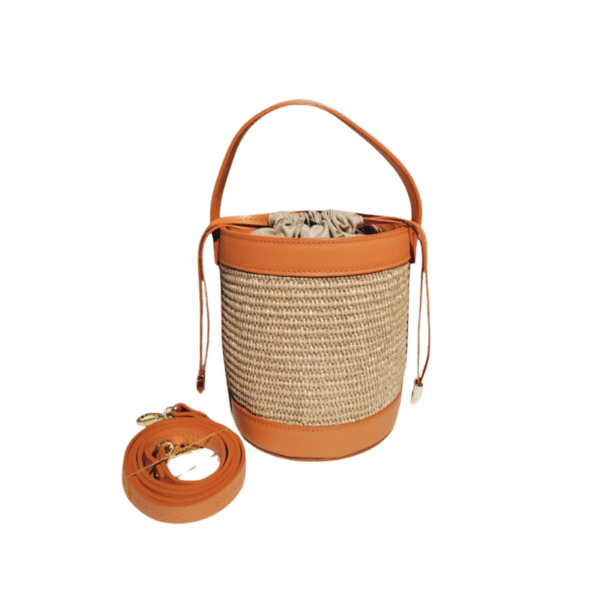 Le Sac à main bandoulière raphia garni cuir-Bleu Ciel présente des bordures en cuir fauve, une poignée en cuir, une fermeture à cordon de serrage et une bandoulière en cuir détachable assortie avec des ferrures dorées placées à côté du sac.