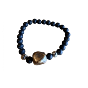 Le Bracelet en billes volcaniques /pierre bleue se compose de perles volcaniques noires mates, de deux accents argentés brillants et d'une grande perle centrale métallique irrégulière dans un arrangement circulaire.