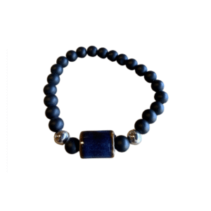 Le Bracelet en billes volcaniques /pierre bleue se compose de perles volcaniques noires rondes, de deux accents argentés brillants et d'une grande pierre rectangulaire bleu foncé, présentée sur un fond blanc.
