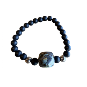 Le Bracelet en billes volcaniques/pierre bleue se compose de perles volcaniques noires, d'une grande perle centrale bleue marbrée et de deux petites touches d'argent, le tout élégamment présenté sur un fond blanc.
