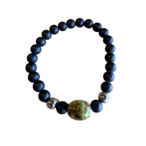 Le Bracelet en billes volcaniques /pierre bleue se compose de perles rondes noires mates, de deux perles argentées brillantes et d'une grande perle centrale brun-vert, le tout sur fond blanc.