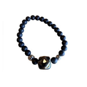 Le Bracelet en billes volcaniques/pierre bleue est composé de perles volcaniques noires, d'une grande pierre centrale bleue irrégulière et de deux petites perles argentées, le tout sur fond blanc.