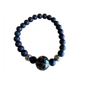 Bracelet en billes volcaniques et pierre bleue, avec perle centrale marbrée et deux perles argentées, présenté sur fond blanc.